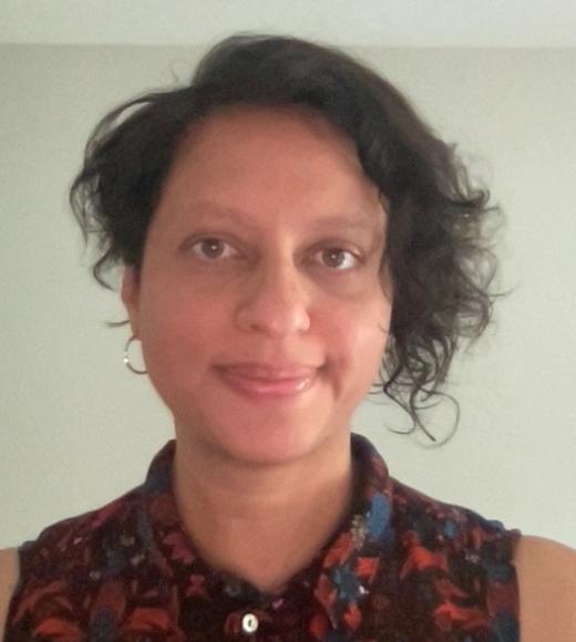 Close-up photo of Beenash Jafri smiling into the camera. She is wearing a collared shirt and has short dark curly hair. 