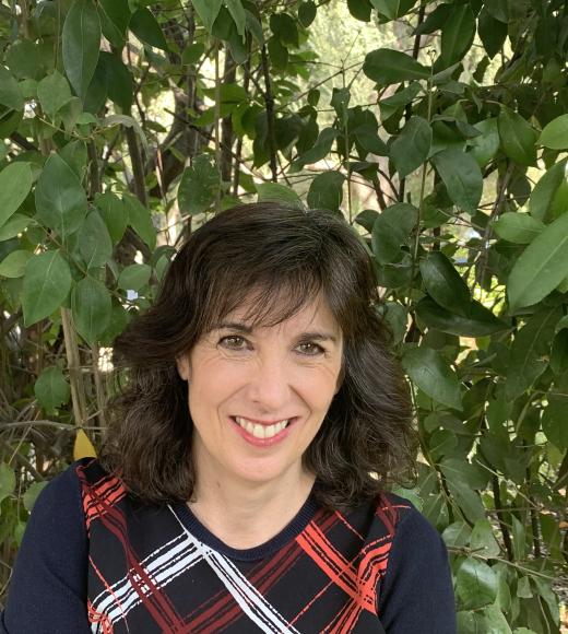 Photo of GSW Chair Kathryn Olmsted - she is smiling and sitting in front of a leafy green background. She is wearing a navy blue sweater with a red and white pattern. 