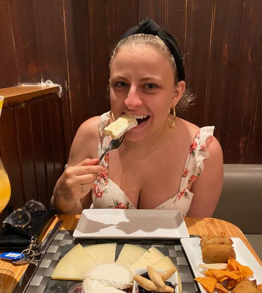 Woman with blonde hair wearing a white dress eating cheese